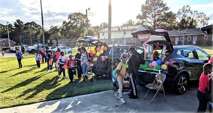 Kids lined up to go trunk or treating in the back of decorated car trunks.