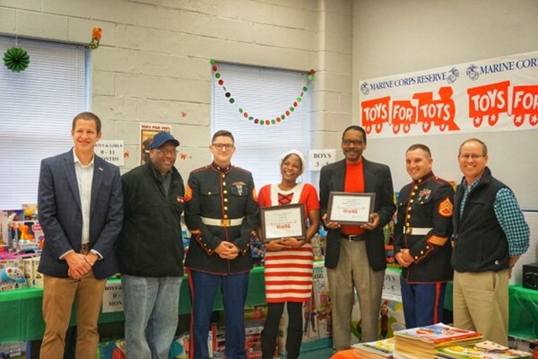 A group of men and women posing in a line. A man and a woman hold two plaques. 