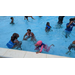 Kids swimming in the pool with life jackets on. 