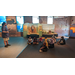 Children sitting on the ground listening to a man talk. 